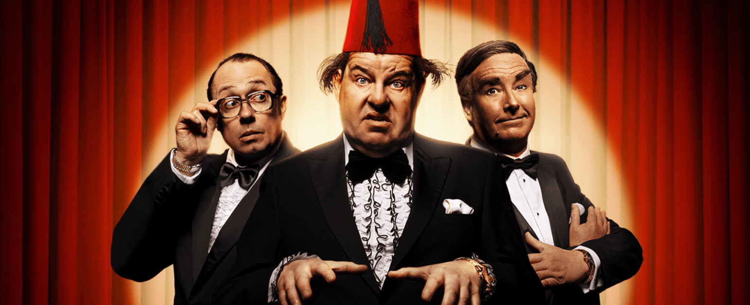 Tommy Cooper, Eric Morecambe and Bob Monkhouse impersonators  in front of a red camera