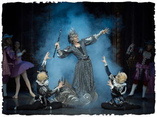 A performer in a black dress in smoke is looked up to by two other performers