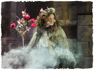 The BEast wearing a cloak with haze in front of him and a rose bush behind him