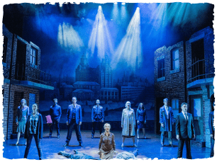 Blue lighting, cast spread across stage under blue lighting