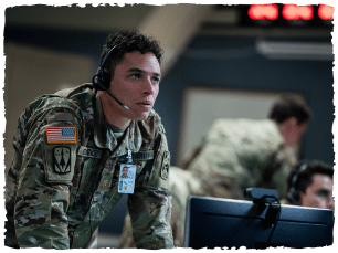 Man in army camos, with headset on stood at a desk