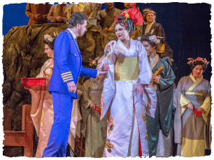 A performer in a blue suit stands next to a performer in a white dress