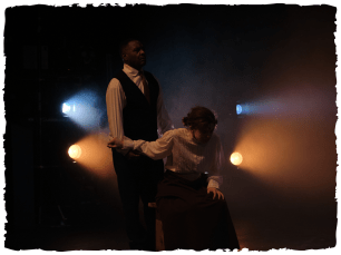 2 people on dark stage, with a few big lights