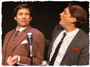 Man in brown suit and man in grey suit, stood in front of a mic
