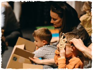 Children wearing animal masks and playing in boxes, with adults helping