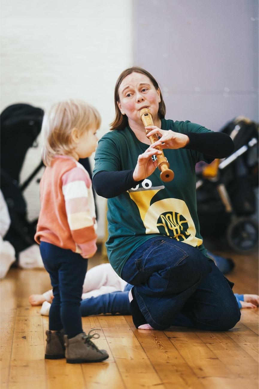 A woman playing the recorder and a child watching