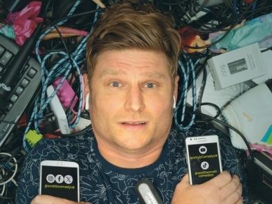 Scott Bennet is spiked blond hair and holding two phones lies on top of a pile of rubbish made from old toys and letters and wiring