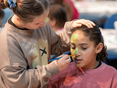One child applying green makeup to another child's face