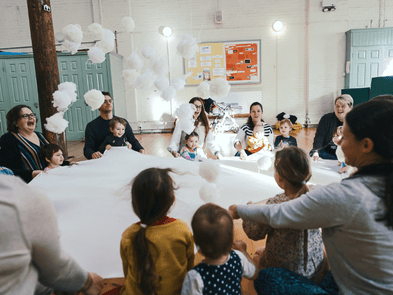 A group of babies and toddles around a white fabric theyre holding onto