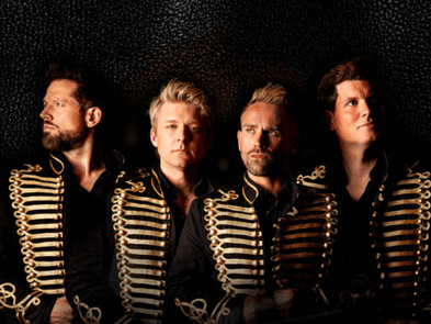 4 men stand in suits in front of a large window on a staircase
