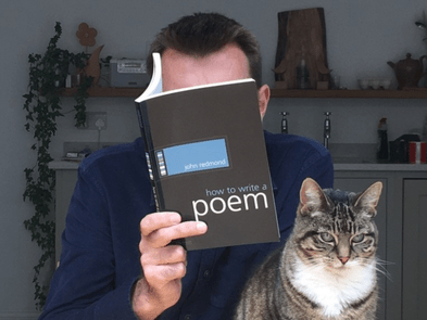 A man reading a book and a cat sat next to him
