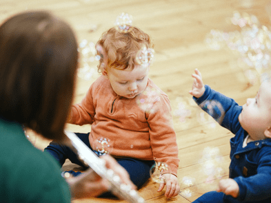A performer playing the flute to babies who are playing with bubbles