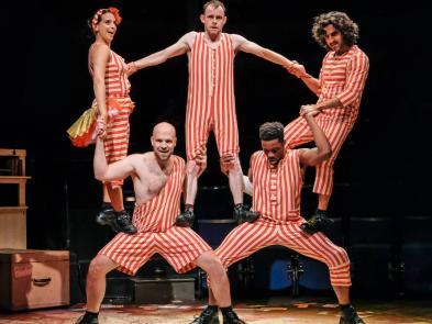 Five Performers in stripey outfits balancing on top of one another